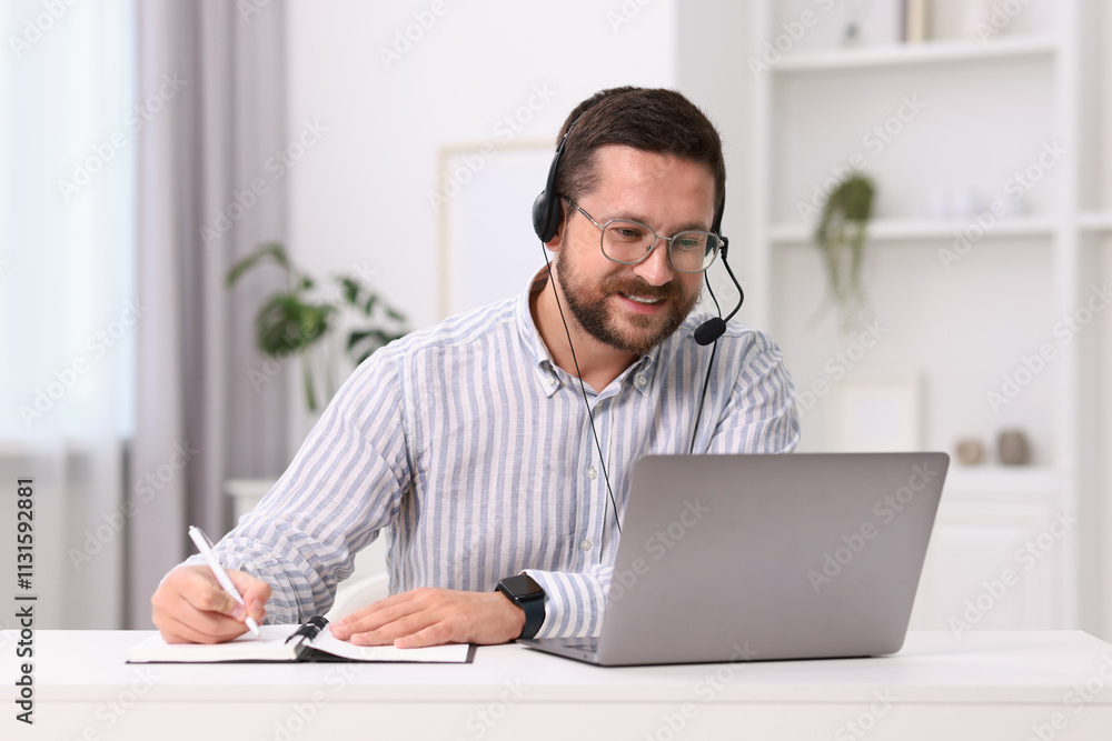 Poster interpreter in headset taking notes while having video chat via laptop at white table indoors