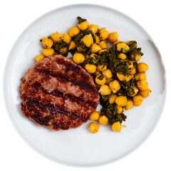 There is plate with hearty lunch on dark checkered tablecloth. Flat fried burger patty cutlet is guaranteed with protein supplement - portion of chickpeas and spinach. Isolated over white background