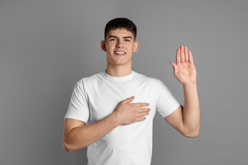 Man making promise with raised hand on grey background. Oath gesture