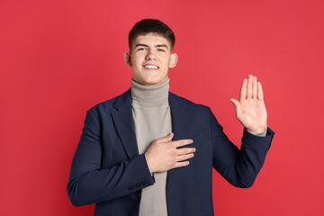 Man making promise with raised hand on red background. Oath gesture