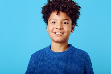 cheerful african american boy with curly hair beaming with joy against a vibrant blue background