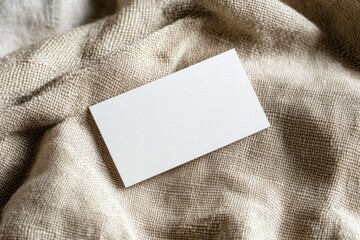 Fototapeta premium Blank business card resting on textured fabric surface under soft lighting in a neutral setting