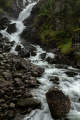 Obraz premium A stunning waterfall flows through a lush forest, tumbling over rocks and surrounded by vibrant greenery. The sound of rushing water blends with the peaceful ambiance, creating a serene natural escape