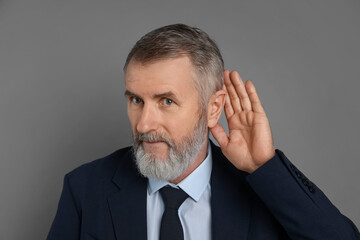 Senior man showing hand to ear gesture on grey background