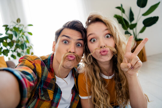 Photo of cute young couple take selfie photo fake mustache v-sign cozy day light spring summer home interior living room