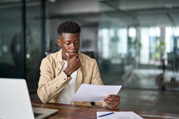 Busy young African business man checking documents working at laptop in office. Serious businessman...