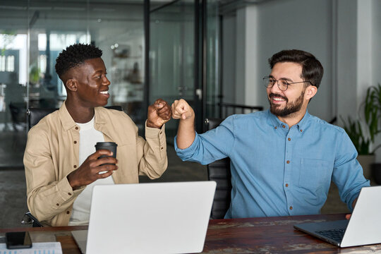 Two happy diverse young professional male employees team giving fist bump at work. African and Hispanic business men buddies colleagues celebrating good collaboration teamwork results together.
