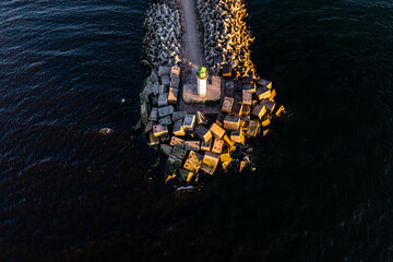 White lighthouse with green top stands on breakwater, surrounded by angular concrete blocks. Low...