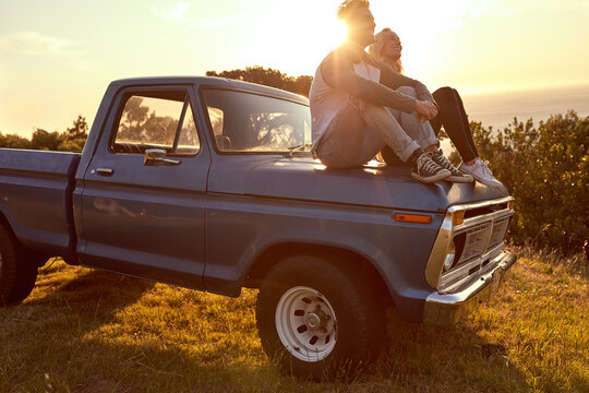 Travel, sunset and couple relax on car for road trip break, holiday adventure and sightseeing together. Lens flare, happy people and view of nature for scenery, weekend vacation or exploring on truck - Powered by Adobe