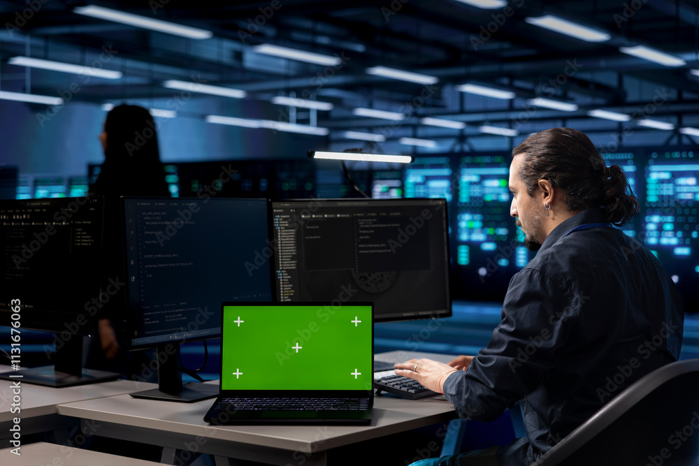 Poster engineer using green screen laptop to oversee servers used for managing databases, hosting websites 