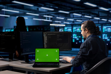 Engineer using green screen laptop to oversee servers used for managing databases, hosting websites...