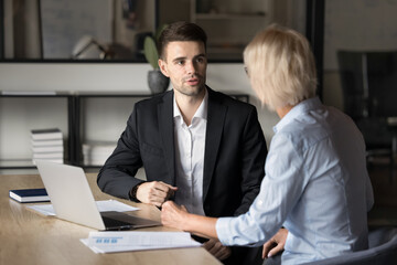 Obraz premium Two businesspeople discuss business-related issues met in office with laptop. Millennial businessman dressed in suit provide information to corporate client, sharing strategy, planning collaboration