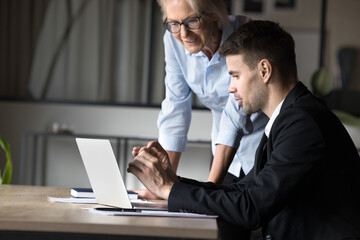 Fototapeta premium Two male female colleague reviewing new corporate software, learn program or business platform, engaged in joint task completion, looking focused, while gaze at laptop screen. Teamwork, modern tech
