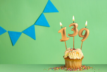 Birthday cupcake with number 139 candle - Green background with blue pennants.