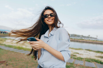 Woman, sunglasses, blue shirt, cell phone, water, windy a woman in sunglasses and a blue shirt...
