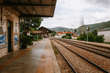 Empty train station platform in Pinhao, alijo, portugal, features traditional azulejo tiles, a wooden station building, and converging railway tracks leading towards the mountainous landscape of vila 
