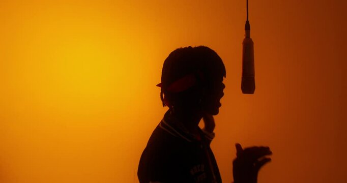 A stylish young man sings into a hanging microphone. Studio video on an orange background
