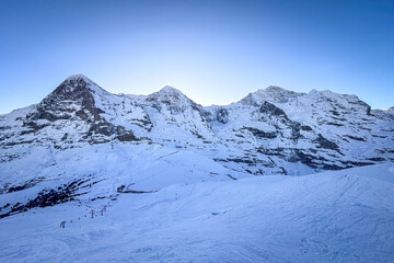 Obraz premium Panoramic view of famous snowcovered Eiger, Moench and Jungfrau mountains (from left to right) in Switzerland in winter early in the morning against blue sky