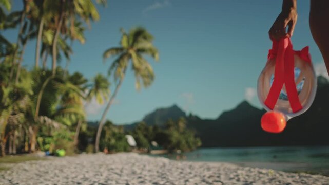 Young woman strolls on a tropical beach, holding a snorkel mask, ready to swim in the crystal blue ocean. Palm trees sway in the warm breeze, creating a serene vacation moment