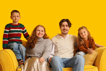 Fototapeta premium Happy family in warm sweaters sitting on sofa near yellow wall