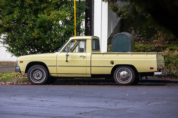 A vintage yellow American SUV 4x4 pickup truck, parked alongside a quiet street, sits near green bushes and trees, embodying a nostalgic and rustic charm in Portland, OR © Hrach