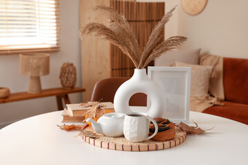 Table with hot tea, poppy buns, pampas grass and autumn leaves in living room