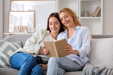 Pretty young woman and her mother with book sitting on sofa at home