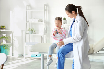 Female pediatrician and cute little girl with inhaler in clinic