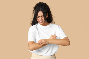Young African-American woman suffering from skin allergy on beige background