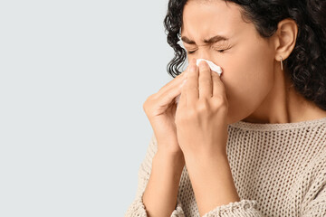 Young African-American woman sneezing in handkerchief on white background. Allergy concept