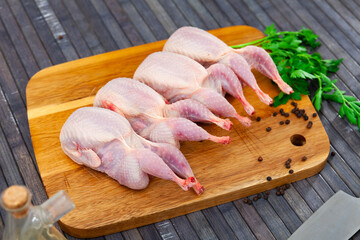 Raw quails on wooden cutting board with parsley stems and peppercorns.