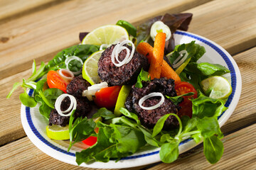 Appetizing black pudding with rice served with vegetables and greens on plate