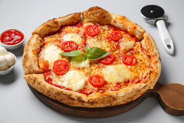 Wooden board with tasty pizza Margarita and bowl of mozzarella cheese on grey background