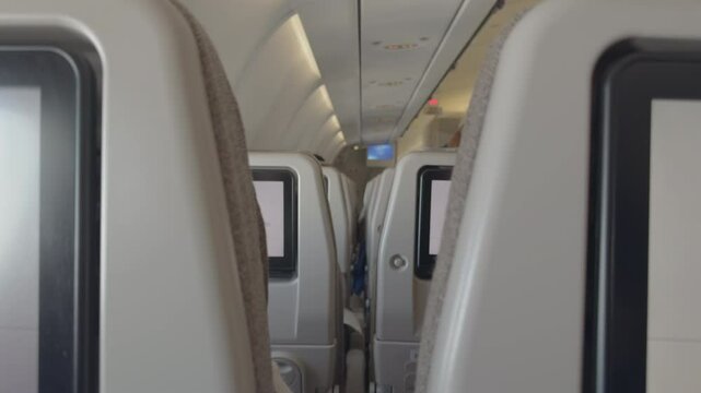 A unique perspective inside an airplane cabin, filmed between two seats, showing rows of passengers and a glimpse of two travelers communicating without revealing their faces.