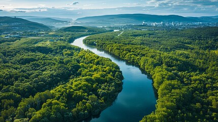 Fototapeta premium Aerial View of a Serpentine River Winding Through Lush Green Forests and Distant Cityscape