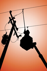 Silhouette of power lineman stand on bucket truck and closing a single phase transformer on energized high-voltage electric power lines.