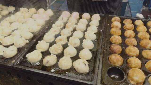 A close-up view of Takoyaki being cooked in a special pan, with shrimp and squid inside.