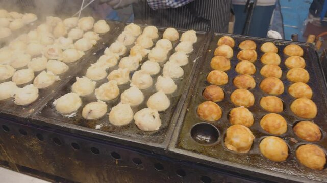 A close-up view of Takoyaki being cooked in a special pan, with shrimp and squid inside.