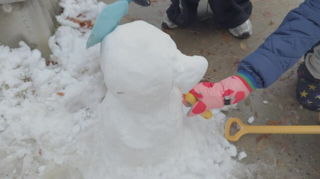 A heartwarming winter scene of a mother and child building a snowman together in a snowy park. The footage focuses on their hands and movements, without showing faces, making it ideal for storytelling