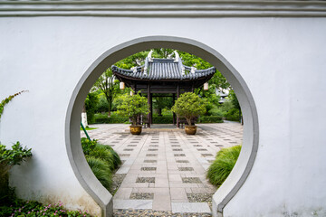 A tranquil view through a moon gate in a Chinese garden. The circular frame encompasses a...