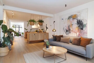 Modern living room with light wood floors, gray sofa, abstract art, and kitchen view.