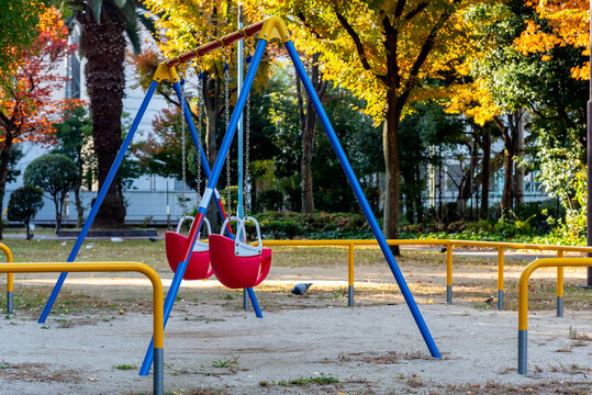 Red swing on playground in colorful authumn public park.