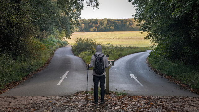 Man Standing at a Crossroads, Deciding Which Path to Take, Decision Making Concept, Two Roads Diverging, Symbolic Choice, Thoughtful Individual Contemplating Direction in Life
