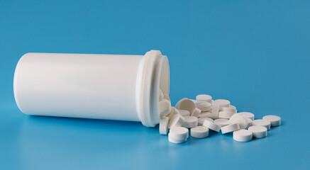 White tablets pour out of a plastic jar. White tablets on a blue background.