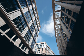 modern business center, high-rise office building with glass facade and columns, skyscraper, blue cloudy sky in sunny summer day, wide angle, urban abstract background, copy space