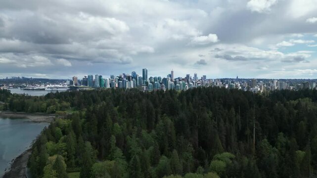 aerial shot going forward over stanley park revealing vancouver city skyline on a cloudy day, british columbia, canada