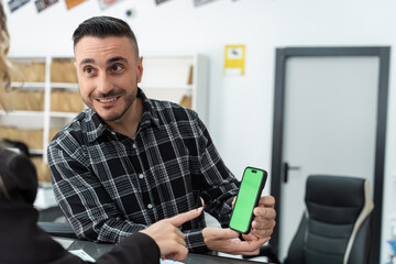 Two colleagues reviewing a new mobile app design on a smartphone with a green screen, perfect for showcasing user interfaces and mobile technology