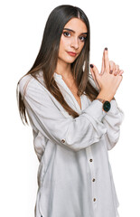 Young beautiful woman wearing casual white shirt holding symbolic gun with hand gesture, playing killing shooting weapons, angry face