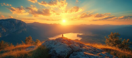 Naklejka premium Majestic sunset over mountains and lake, lone hiker on peak.