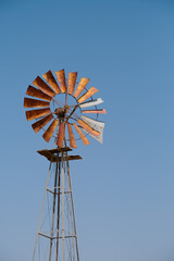 Old windmill standing tall against a clear blue sky in Namibia. Its weathered metal blades evoke a sense of timelessness and rural charm in the arid landscape.